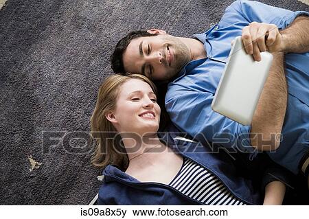 Stock Photo - Young couple lying on floor with electronic book. Fotosearch