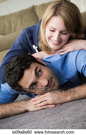 Stock Image - Young couple lying on floor, woman on top of man. Fotosearch