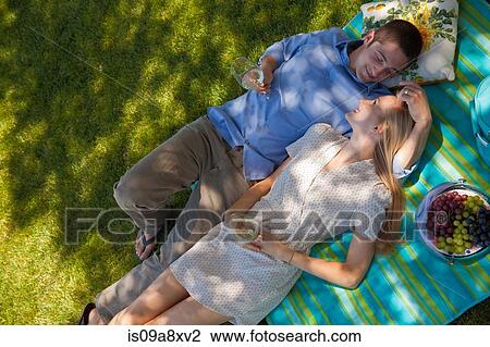 Stock Image - Young couple lying on picnic blanket, overhead view. Fotosearch