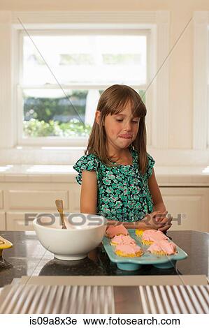Stock Image - Young girl looking at cupcakes, licking lips. Fotosearch