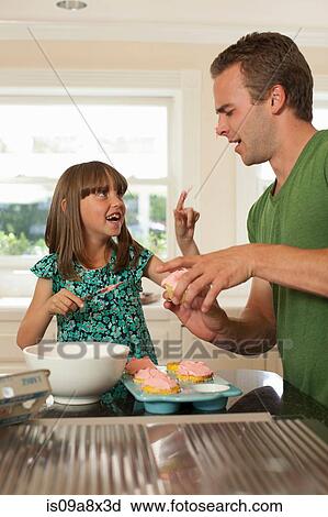 Stock Image - Young girl putting icing on older brother's nose. Fotosearch