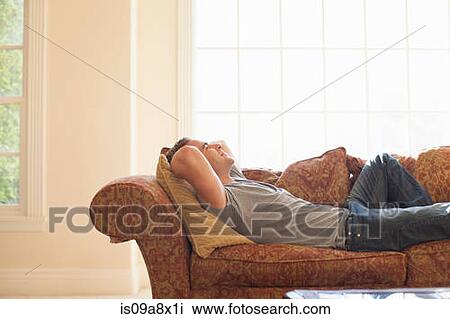 Young man lying on sofa with hands behind head View Large Photo Image Stock Image - Young man lying on sofa with hands behind head. Fotosearch