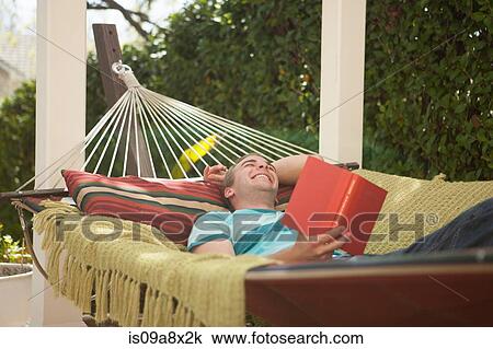 Stock Image - Young man reading book in hammock, laughing. Fotosearch
