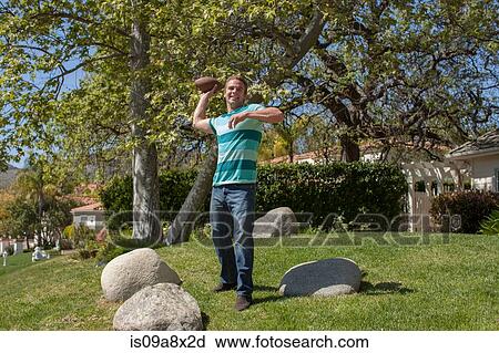 Stock Image - Young man throwing american football in garden. Fotosearch