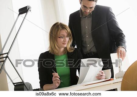 Stock Image - Young office workers looking through paperwork. Fotosearch
