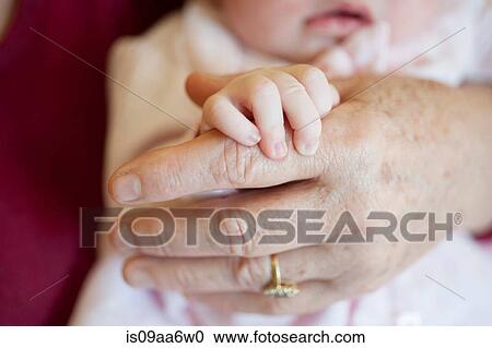 Stock Image - Baby girl holding senior woman's hand, close up. Fotosearch