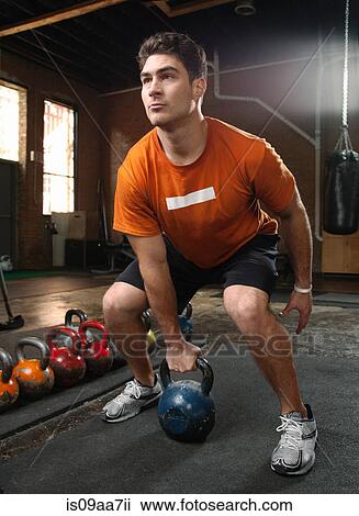 Stock Image - Bodybuilder lifting kettlebells in gym. Fotosearch