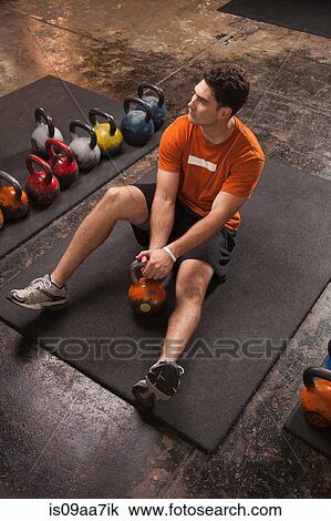 Stock Image - Bodybuilder resting on exercise mat in gym. Fotosearch