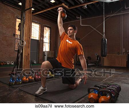 Stock Image - Bodybuilder using kettlebells in gym. Fotosearch