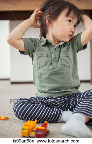 Stock Photo - Boy sitting on floor with hands in hair. Fotosearch