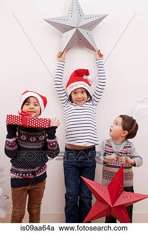 Stock Image - Children holding up Christmas decorations. Fotosearch
