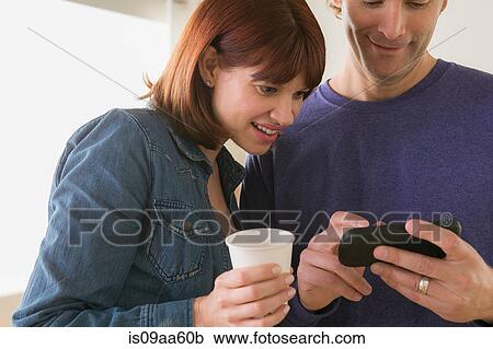 Stock Image - Close up of couple looking at mobile phone. Fotosearch