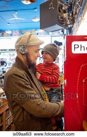 Stock Image - Father holding young son by public telephone. Fotosearch