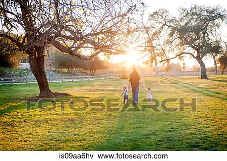 Stock Photo - Father walking with son and daughter in sunlit field. Fotosearch