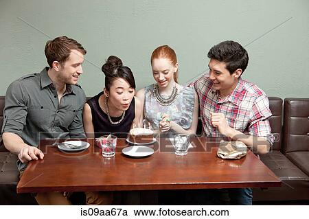 Stock Image - Four friends celebrating birthday in restaurant. Fotosearch