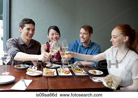 Stock Image - Four friends toasting white wine in restaurant. Fotosearch