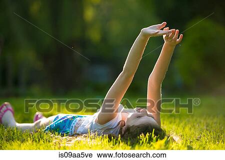 Girl lying on grass with arms raised View Large Photo Image Stock Image - Girl lying on grass with arms raised. Fotosearch