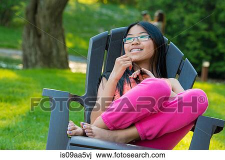 Girl sitting on garden chair looking away smiling View Large Photo Image Stock Image - Girl sitting on garden chair looking away smiling. Fotosearch