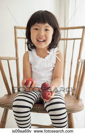 Girl sitting on wooden chair holding apples, portrait View Large Photo Image Stock Photo - Girl sitting on wooden chair holding apples, portrait. Fotosearch