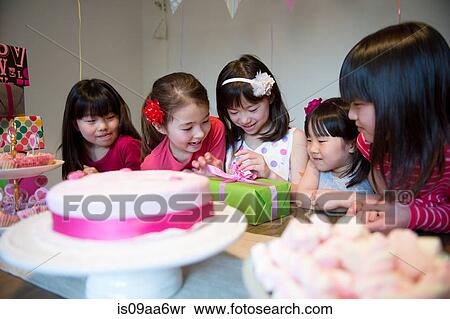 Stock Photography - Girl unwrapping birthday present at party. Fotosearch