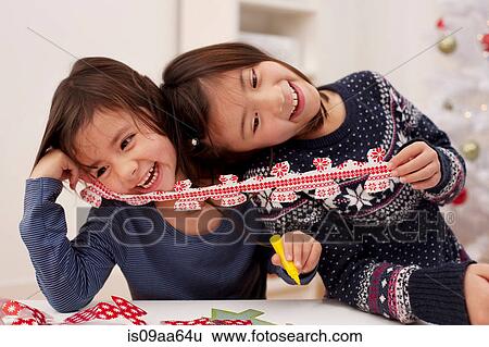 Stock Photograph - Girls holding Christmas decorations, laughing. Fotosearch