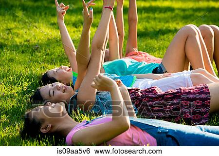Girls lying on grass with arms raised, pointing View Large Photo Image Stock Photograph - Girls lying on grass with arms raised, pointing. Fotosearch