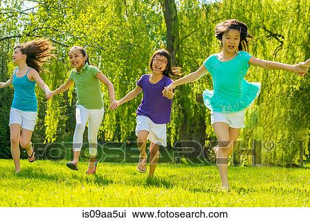 Stock Image - Girls running in park holding hands. Fotosearch