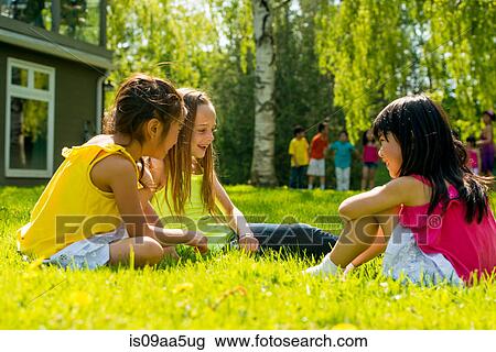 Stock Image - Girls sitting on grass talking. Fotosearch