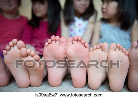 Stock Photo - Girls sitting together with barefeet in a row. Fotosearch