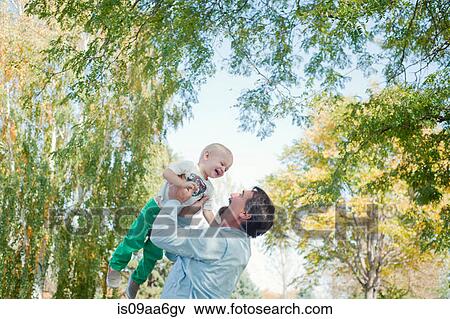 Stock Photo - Grandfather lifting grandson in park. Fotosearch