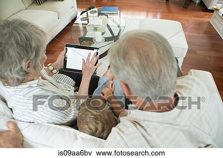 Stock Photo - Grandparents showing boy digital tablet on sofa. Fotosearch