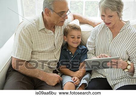 Stock Photograph - Grandparents showing boy digital tablet on sofa. Fotosearch