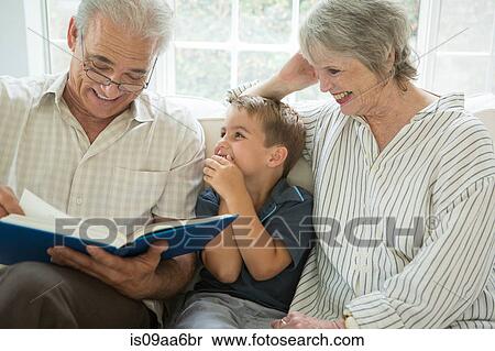 Stock Photography - Grandparents showing boy photo album on sofa. Fotosearch