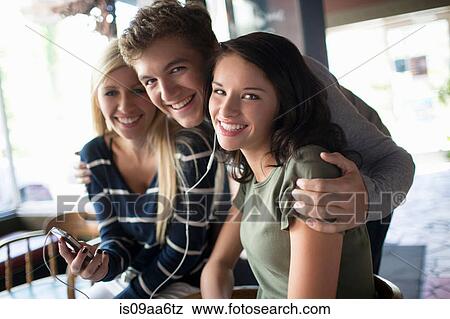 Group of friends sharing earphones in coffee house View Large Photo Image Stock Photo - Group of friends sharing earphones in coffee house. Fotosearch
