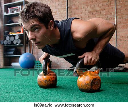 Stock Image - Male bodybuilder doing press up using kettlebells. Fotosearch