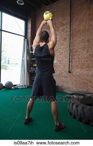 Stock Image - Male bodybuilder lifting kettlebells in gym. Fotosearch