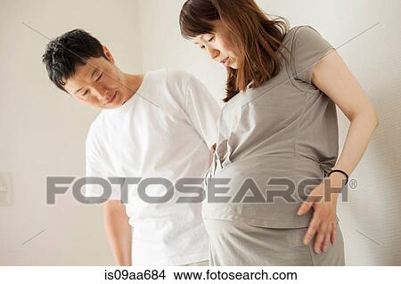 Picture - Man and pregnant woman looking down at stomach, portrait. Fotosearch