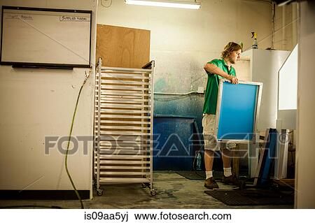 Stock Image - Man holding frame in screen print workshop. Fotosearch