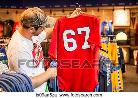 Man holding up t-shirt in store View Large Photo Image Stock Image - Man holding up t-shirt in store. Fotosearch