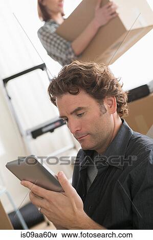 Man looking at digital tablet whilst moving home View Large Photo Image Stock Photo - Man looking at digital tablet whilst moving home. Fotosearch