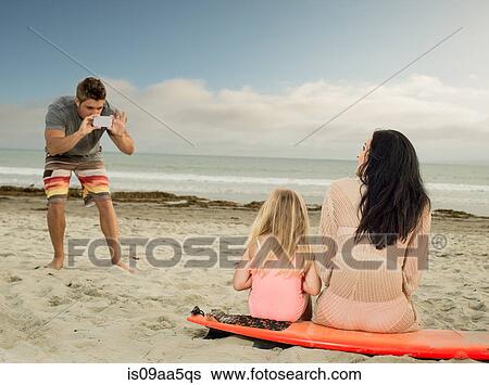 Man photographing family as the sit on a surfboard View Large Photo Image Stock Photograph - Man photographing family as the sit on a surfboard. Fotosearch