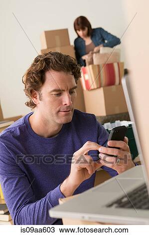 Stock Image - Man texting on cellphone whilst moving house. Fotosearch