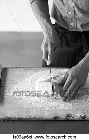 Stock Image - Mid adult baker slicing fresh dough. Fotosearch