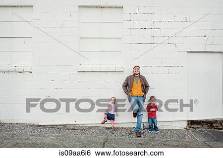 Stock Photograph - Mid adult man and son and daughter leaning against wall, portrait. Fotosearch