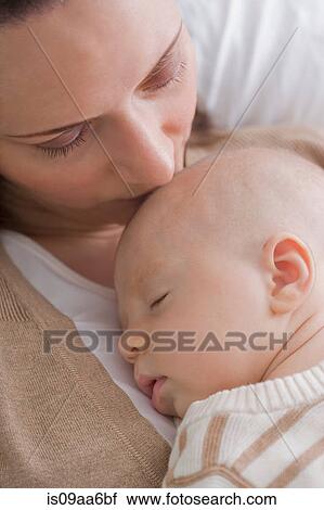 Stock Image - Mid adult mother kissing baby boy. Fotosearch