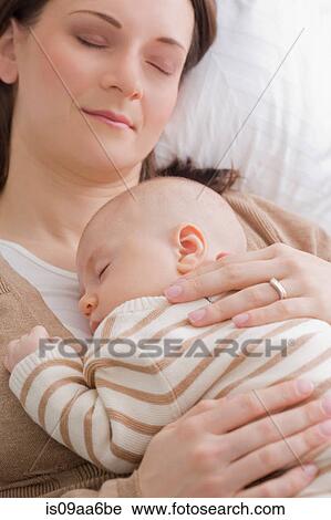 Stock Image - Mid adult mother resting with baby boy. Fotosearch