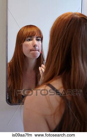 Picture - Mid adult woman applying lip gloss in mirror. Fotosearch