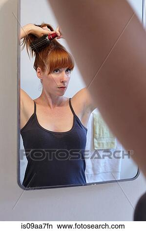 Picture - Mid adult woman brushing hair in mirror. Fotosearch