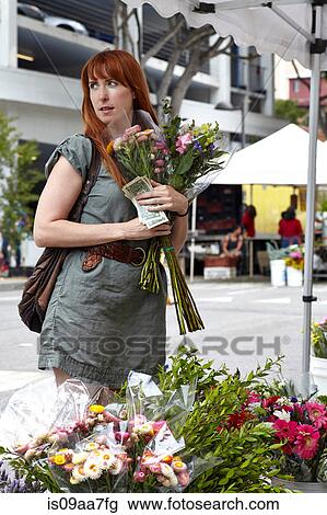 Stock Image - Mid adult woman buying flowers from stall in city. Fotosearch