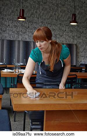 Stock Photograph - Mid adult woman cleaning table in restaurant. Fotosearch